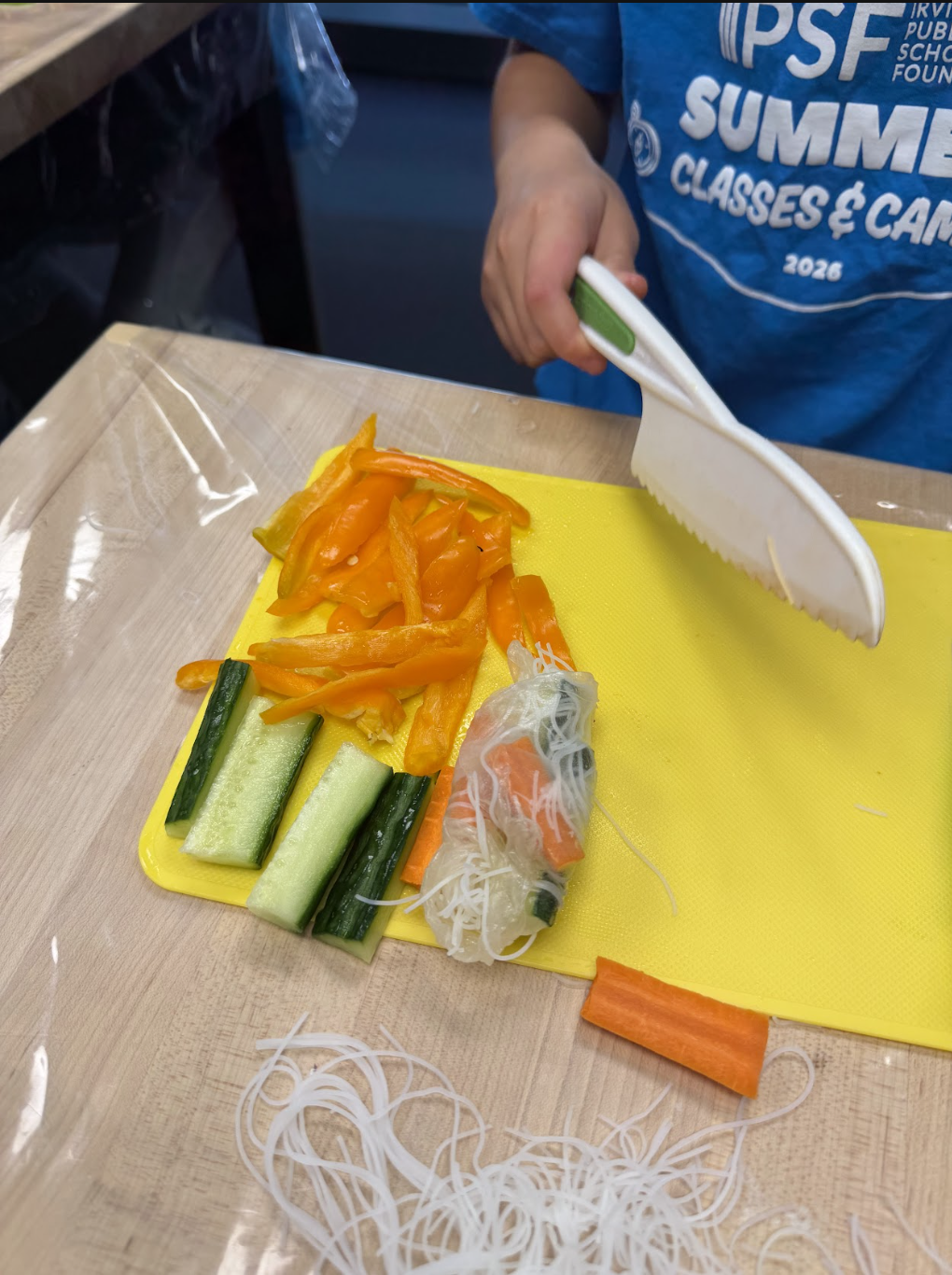 An IPSF summer camper slices vegetables with a kids' knife at the Boys Who Cook workshop