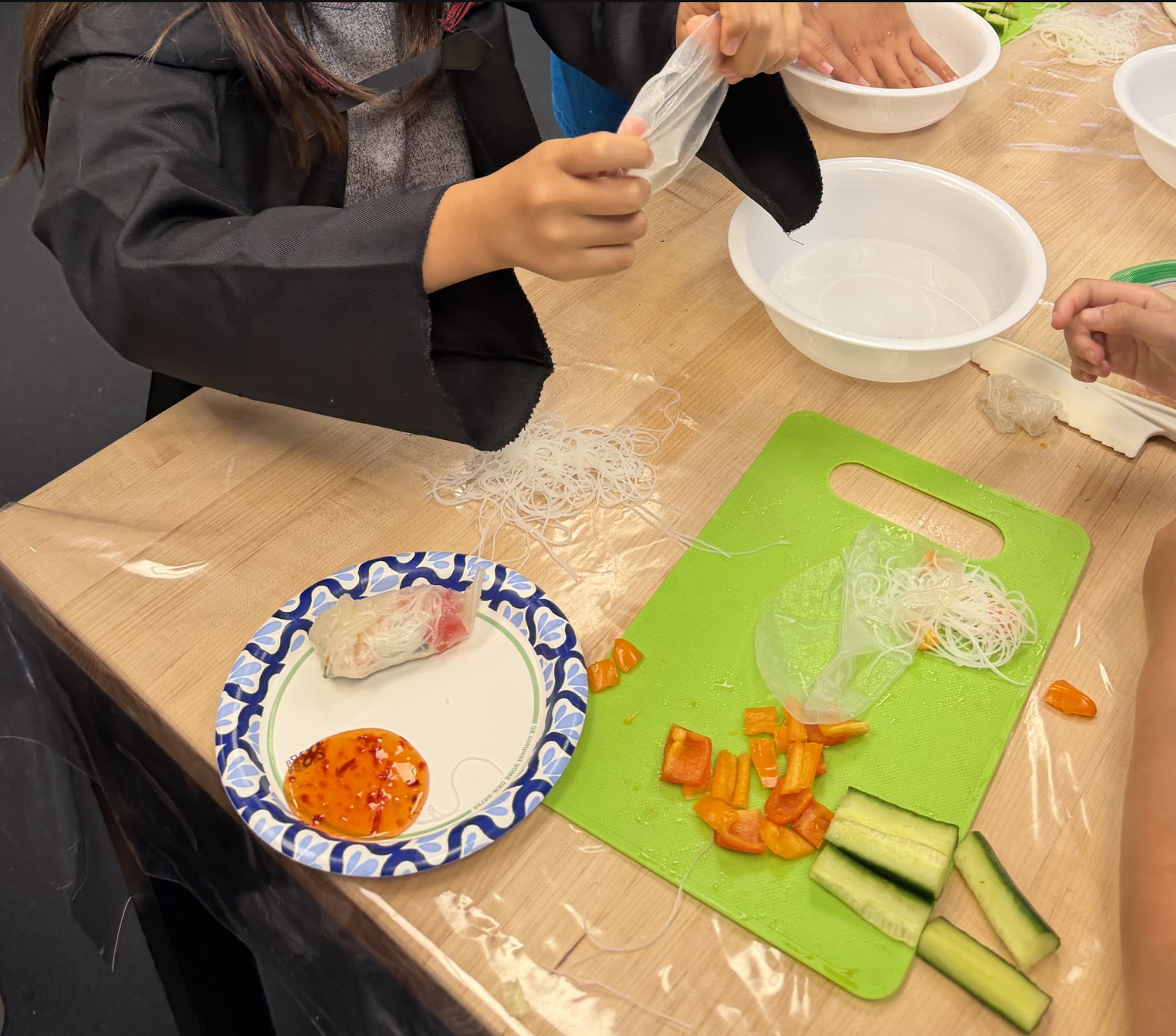 A student carefully wraps fresh vegetables and rice noodles in a softened rice paper sheet
